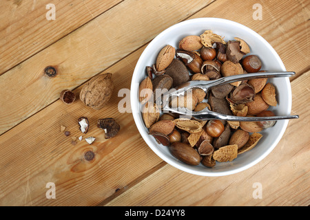 Nussmischung in einer weißen Schüssel mit einem Metall Nussknacker, fotografiert auf altem Holz Stockfoto