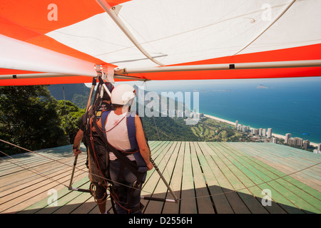 Brasilien, Rio, Tijuca-Wald, Tandem-Drachenflieger, die sich auf den Start am Pedra Bonita-Felsen über dem Strand von Sao Conrado vorbereiten. Blick auf den Strand und den Atlantischen Ozean Stockfoto