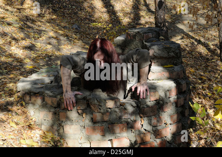 Horror-Frau in einem alten Backstein-Brunnen, kriechen Stockfoto