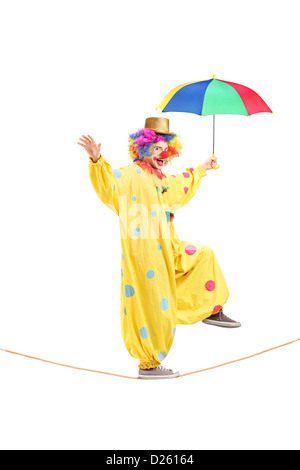 In voller Länge Portrait eines glücklichen männlichen Clowns mit Regenschirm zu Fuß auf einem Seil isoliert auf weißem Hintergrund Stockfoto