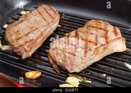 Zwei Striploin (oder New York) Steaks Grillen in einer Pfanne mit Knoblauch und Rosmarin Stockfoto
