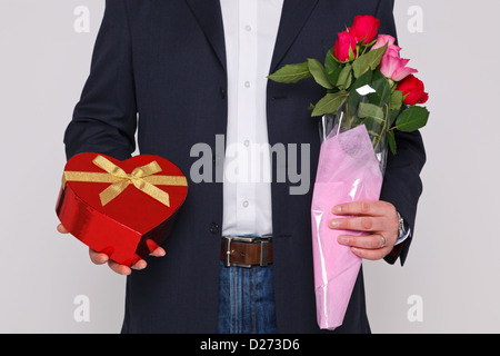 Mann, der einen Blumenstrauß und eine herzförmige Schachtel Pralinen. Stockfoto