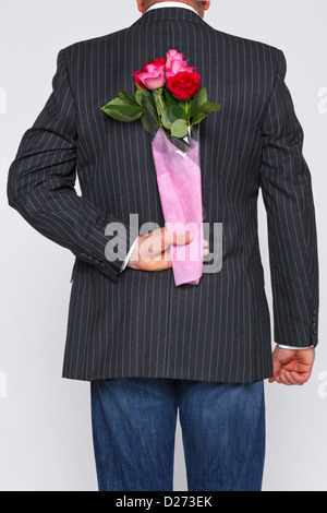 Ein Mann mit einem Rosenstrauß hinter seinem Rücken, die Blüten sind eine Überraschung für jemanden. Stockfoto