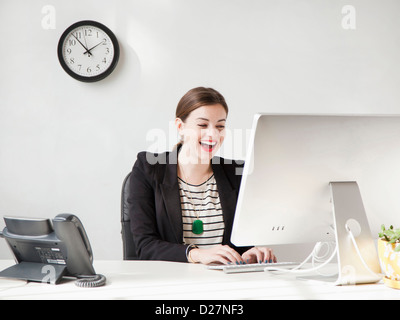 Studioaufnahme von junge Frau am Computer arbeiten und lachen Stockfoto