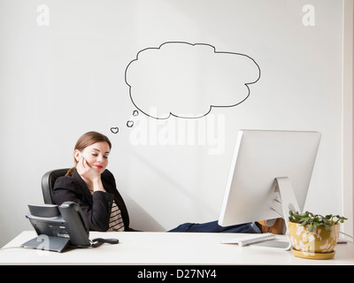 Studioaufnahme der jungen Frau, die Arbeiten am Schreibtisch mit dachte Bläschen neben ihrem Kopf Stockfoto