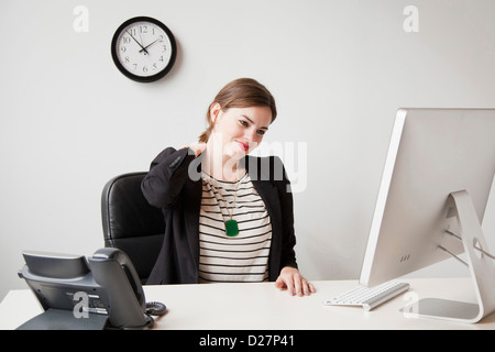 Studioaufnahme jungen Frau im Büro arbeiten und den Hals berühren Stockfoto