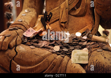 Es ist ein Foto von Close up auf Münzen und Banknoten, die auf die Hände der Statue des Buddha in einem Tempel oder Museum in China. Stockfoto