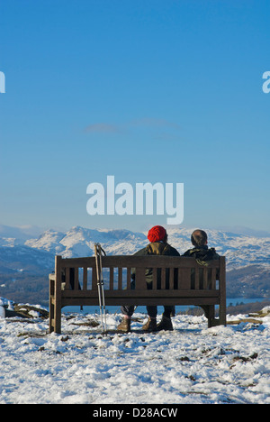 Zwei Wanderer sitzen auf einer Bank am Orrest Head mit Blick auf Lake Windermere und die Langdale Pikes, Cumbria, England UK Stockfoto