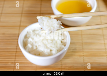 Reis auf Bambus Matte Closeup mit Stäbchen Stockfoto