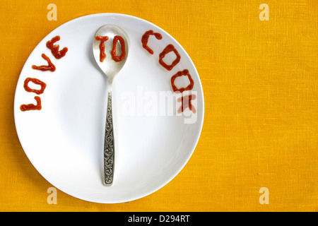 die Liebe zum Kochen von Tomatensauce auf weißen Teller und silbernen Löffel geschrieben Stockfoto