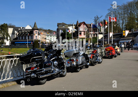 Motorräder ("Harley Davidson") geparkt auf einem Bürgersteig in Bagnoles de Frankreichunter, einzigartigen Spa Resort im Westen Frankreichs und Touristen. Stockfoto