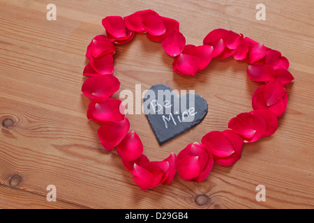 Rote Rosenblätter und Schiefer in Form eines Herzens mit einer romantischen Liebesbotschaft "Be Mine" Stockfoto