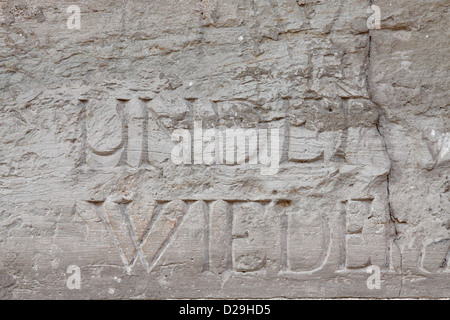 Fragment der Innenwand der alten katholischen Kathedrale. Es gibt Wörter und Buchstaben an der Wand in lateinischer Sprache geschnitzt. Stockfoto