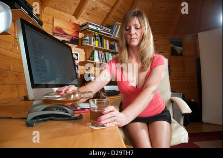 Weiblich, Alkohol Problem Büro Arbeiter gießt aus einer Flasche gehalten in ihrer Schreibtischschublade Stockfoto