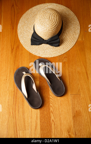 Ein paar lässige Strandsandalen und Stroh Strandhut auf einem Holzdeck Stockfoto