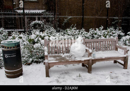 London, UK. 18.01.13. Ein Schneemann mit einer Flasche Wein sitzt auf einer Parkbank in der Nähe von Tottenham Court Road, als Schnee im Zentrum von London fällt. Stockfoto