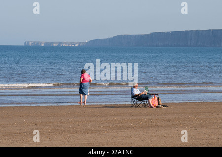 Urlaub Paar auf ruhigen Sandstrand (Paddeln sitzen Entspannen in der Sonne) durch ruhige Blaue flache Meer - South Bay, Scarborough, Yorkshire, England, Großbritannien Stockfoto