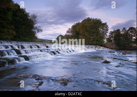 Malerische, Abend, ländliche Landschaft von Wasser & tumbling Über & down Wehr Schritte - River Wharfe, Burley in Bösingen, Yorkshire, England, UK. Stockfoto