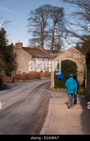 Ansicht der Rückseite des Paar an Land gehen, Wandern am Straßenrand Pflaster, durch ländlichen, ruhigen malerischen Dorf - Bolton Abbey, North Yorkshire, England, UK. Stockfoto