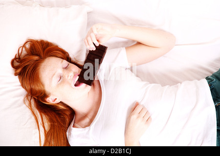 Eine junge rothaarige Frau im Bett Schokolade zu essen. Stockfoto