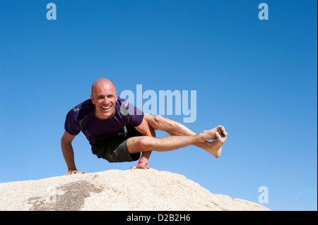 Der Mensch in der Yoga-Pose Astavakrasana im freien balancieren auf einem großen Stein. Stockfoto