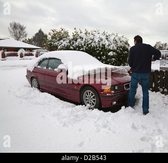 Ein Mann mit einem Besen, um Tiefschnee aus seinem Auto in der Einfahrt zu Bürsten. Stockfoto