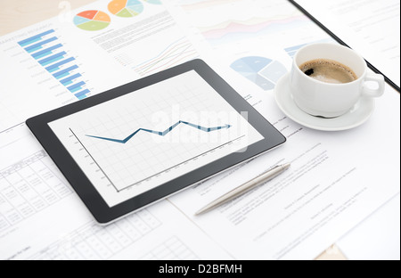 Desktop mit schlechten statistischen Bericht über eine moderne digital-Tablette, einige Papiere mit Diagrammen und Grafiken und mit einer Tasse Kaffee. Stockfoto