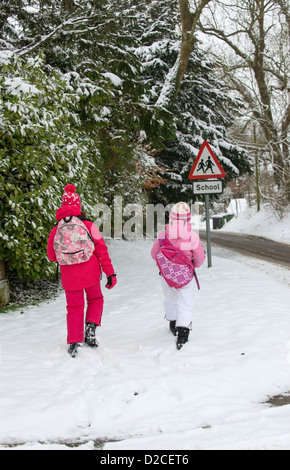 Kinder gehen zur Schule entlang einer Schnee bedeckt Straße mit einem Schild der Schule Stockfoto