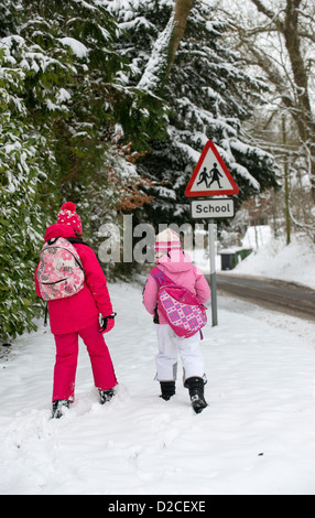 Kinder gehen zur Schule entlang einer Schnee bedeckt Straße mit einem Schild der Schule Stockfoto