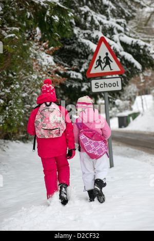 Kinder gehen zur Schule entlang einer Schnee bedeckt Straße mit einem Schild der Schule Stockfoto