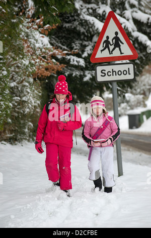 Kinder gehen zur Schule entlang einer Schnee bedeckt Straße mit einem Schild der Schule Stockfoto