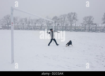 Ein Haustier soll einen gelben Tennisball für seinen elsässischen Hund an einem verschneiten Tag in London Südpark zu werfen. Während einer längeren Kälteperiode des schlechten Wetters fiel Schnee kontinuierlich auf das Kapital am Sonntag, so dass Familien die Möglichkeit, die trostlosen Bedingungen genießen hier in Ruskin Park im Stadtteil Lambeth. Seinen rechten Arm, der Mann Pausen vor den Ball Weg unter einem Fußball Torpfosten pitching zurückziehen Bestandteil eines Fußballplatzes durch lokale Teams verwendet. Der Hund wartet auf die Flugbahn des Balls, bevor in die Ferne in der Nähe von Edwardian Periode Häuser unter 100 Jahre alten Eschen abreißen Stockfoto