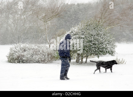 Mann mit Schnee bedeckt, während des Gehens eines Hunds in einem Schneesturm in einem Park. Stockfoto