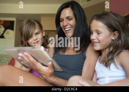 Mutter und ihren beiden Töchtern sitzen im Wohnzimmer Blick auf Ipad zusammen und lachen. Stockfoto