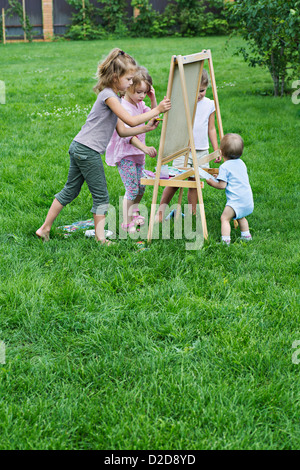 Drei Mädchen und ein Kleinkind im Freien auf einer Staffelei malen Stockfoto