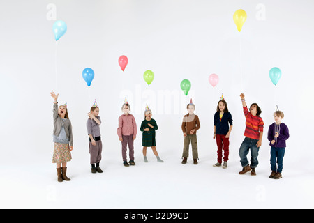 Eine Gruppe von meist langweilig suchen Kinder halten Ballons und tragen Partyhüte Stockfoto
