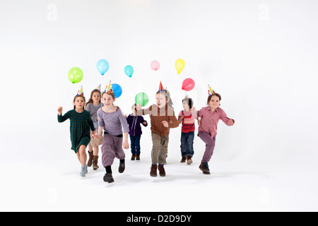 Eine Gruppe von Kindern in Partyhüte und tragenden Ballons vorwärts laufen Stockfoto