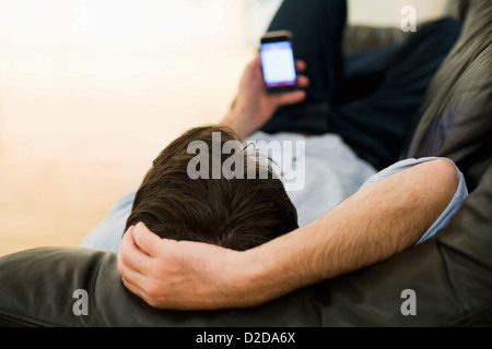 Ein Mann liegt auf dem Sofa, Blick auf Smartphone, Blick von oben auf Kopf Stockfoto