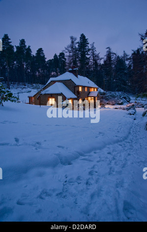 Weihnachtskarte-Bild einer verschneiten Hütte in der Nacht mit den Lichtern auf und Spuren im Schnee Stockfoto