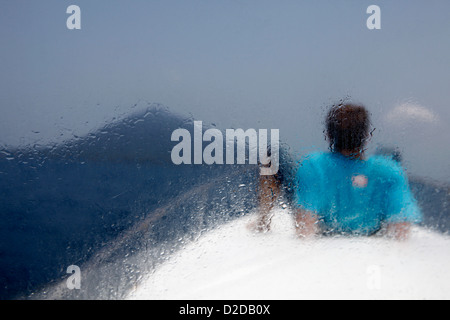 Ein Mann, liegend auf einem Boot Blick auf Vulkan Krakatau, Rückansicht, gesehen durch Fenster Stockfoto