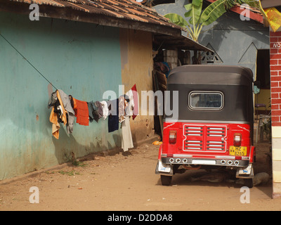 Helles rotes Tuktuk neben Blau geparkt - lackiert lokalen Haus mit Waschmaschine trocknen auf Zeile außerhalb in Negombo, Sri Lanka Stockfoto