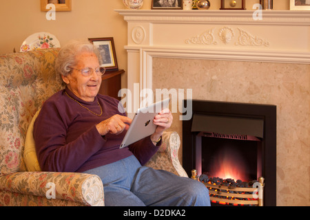 Ältere Frau Rentner mit Brille auf Apple Ipad Tablet zu Hause relaxen am Stuhl Computerspiel Stockfoto