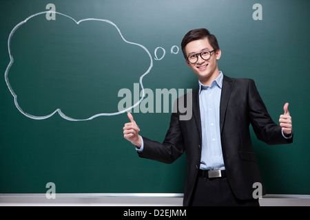 Humorvolle männliche Lehrer tun Daumen oben im Klassenzimmer Stockfoto