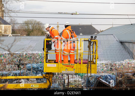 Johnstone, Renfrewshire, Schottland, Großbritannien, Dienstag, Januar 2013. Network Rail Engineers untersuchen die Oberleitungskabel nach einem Brand in der WRC-Recyclingfabrik auf Schäden, die im Hintergrund zu sehen sind und zu Annullierungen, Verzögerungen und Überarbeitungen der Zugdienste auf der Strecke zwischen dem Hauptbahnhof Glasgow und Ayr führen Stockfoto