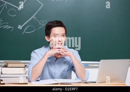 Fröhliche männliche Lehrer Hand am Kinn im Klassenzimmer Stockfoto