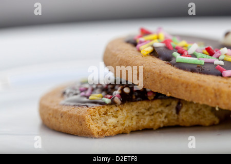 Ein paar bunte Kekse auf einem Teller, auf von ihnen gebissen. Stockfoto