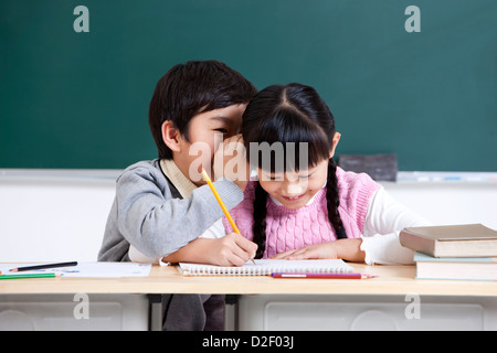 Fröhliche Schulkinder Flüstern im Klassenzimmer Stockfoto
