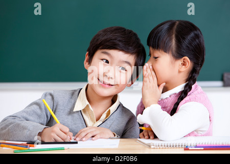 Fröhliche Schulkinder Flüstern im Klassenzimmer Stockfoto