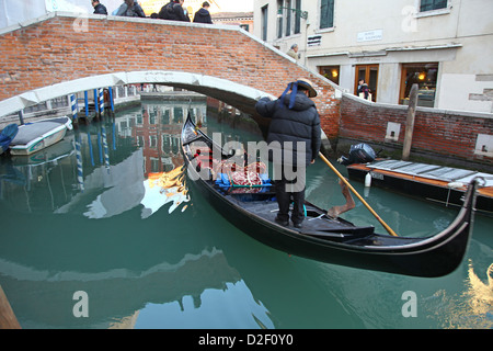 Ein Gondoliere auf einer Gondel Boot Navigation unter einer Brücke auf einen kleinen Kanal in Venedig im winter Stockfoto