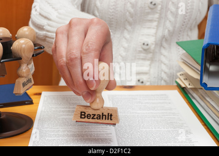 ein Stempel mit der deutschen Aufschrift bezahlt wird in der Hand gehalten. Stockfoto